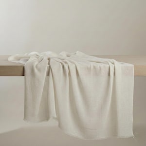 May include: A soft, off-white rectangular throw blanket with a fine, lightweight knit texture and delicate frayed edges. The fabric drapes naturally, showcasing a neutral, solid color and a consistent, semi-sheer weave throughout the entire piece.