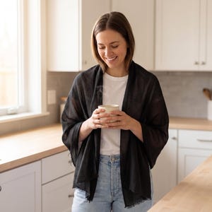 K&ouml;nnte beinhalten: Ein leichter schwarzer Schal mit weicher, halbtransparenter Textur und ausgefransten Kanten, der &uuml;ber die Schultern drapiert ist. Der Schal wird mit einem schlichten wei&szlig;en T-Shirt und einer hellblauen Jeans kombiniert f&uuml;r einen Look.