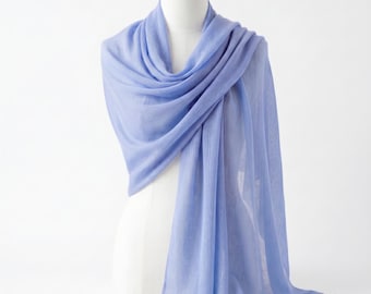 May include: A lightweight periwinkle blue scarf draped over a mannequin. The scarf features a soft, semi-sheer texture with fine, delicate fabric folds that create a gentle, flowing appearance. The edges of the scarf have a subtle, frayed fringe.