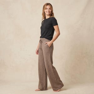 Może przedstawiać: Czarny t-shirt z krótkim rękawem i okrągłym dekoltem w połączeniu ze spodniami z szerokimi nogawkami w kolorze taupe. Spodnie mają wysoki elastyczny pas z dopasowanym sznurkiem do ściągania oraz kieszenie boczne o luźnym kroju.