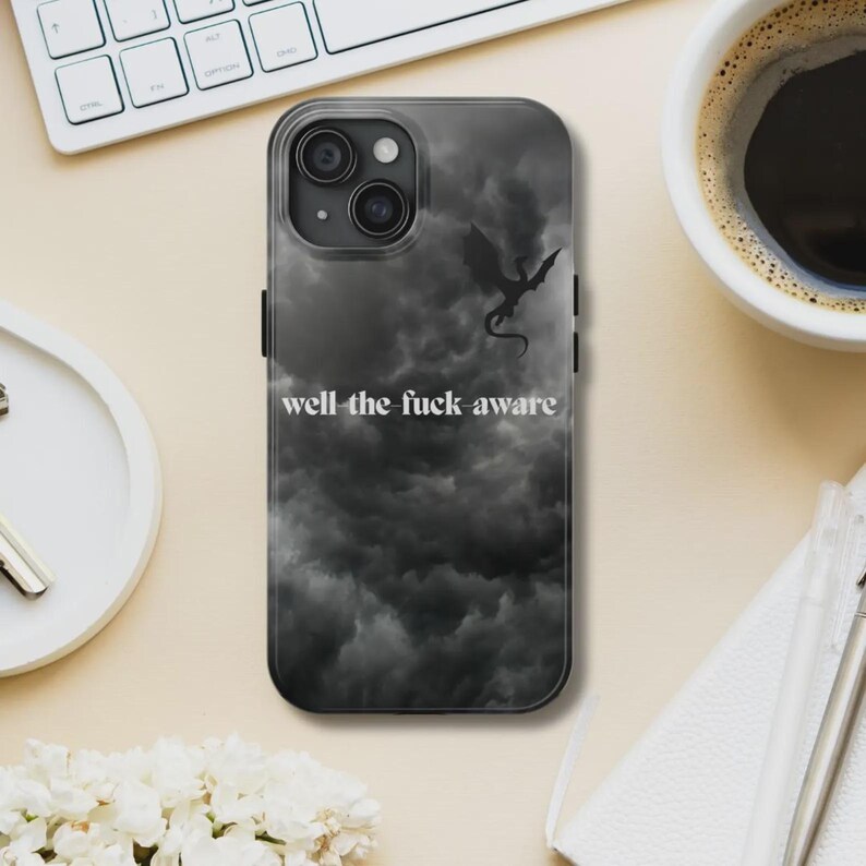 K&ouml;nnte beinhalten: Schwarze Handyh&uuml;lle mit einem dunklen, bew&ouml;lkten Himmel-Design und einer Drachensilhouette. Der Text "well the fuck aware" ist wei&szlig; gedruckt. Die Handyh&uuml;lle liegt auf einer hellen Oberfl&auml;che.