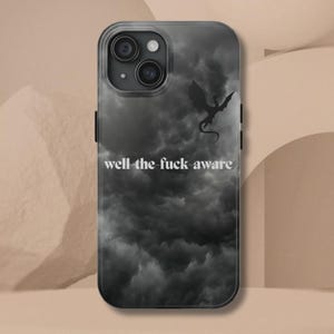 K&ouml;nnte beinhalten: Transparente Handyh&uuml;lle mit einem Design eines dunklen, bew&ouml;lkten Himmels und einer Drachensilhouette. Der Text "well the fuck aware" ist in Wei&szlig; gedruckt. Die H&uuml;lle hat einen schwarzen Rand und bedeckt R&uuml;ckseite und Seiten des Telefons.