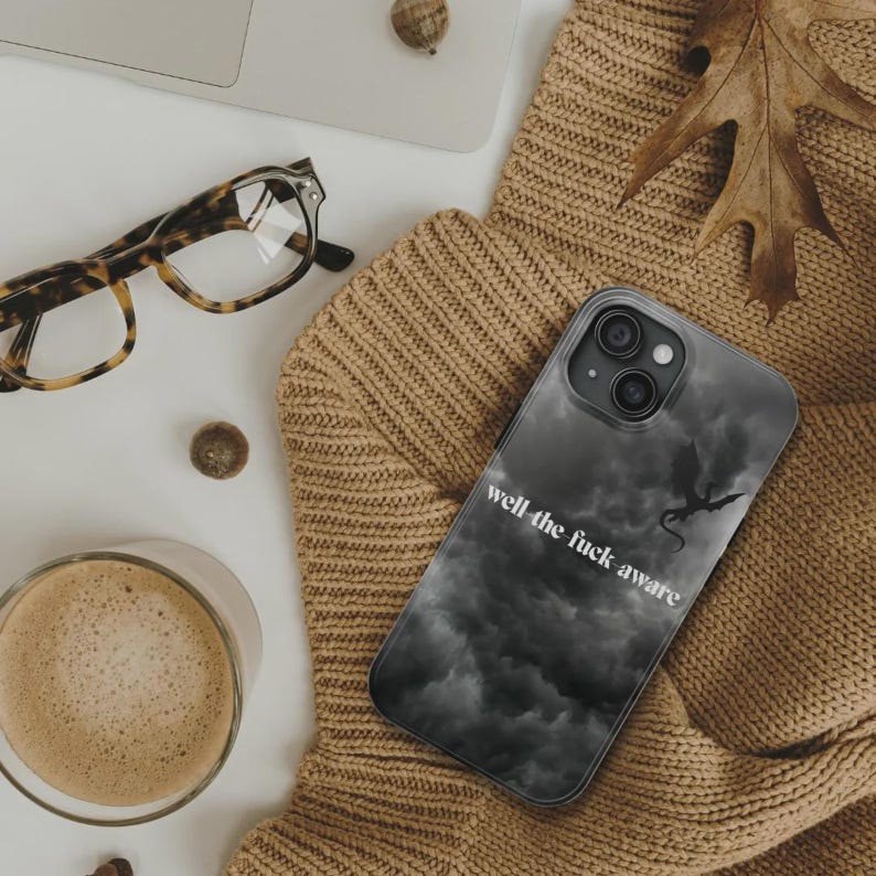 K&ouml;nnte beinhalten: Smartphone-H&uuml;lle mit dunkelgrauem Wolkenmuster und Drachensilhouette. Der Text "well the fuck aware" ist wei&szlig; aufgedruckt. Die H&uuml;lle liegt auf einem beigefarbenen Pullover.
