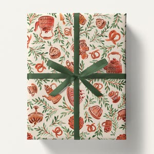 May include: Gift-wrapped package with cream-colored paper featuring a watercolor pattern of teapots, pretzels, and pastries in shades of brown and red, accented with green foliage. A dark green ribbon and bow secure the package.