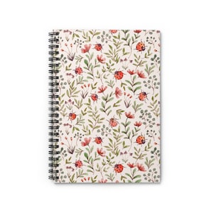 May include: A spiral-bound notebook featuring a cream-colored cover adorned with a repeating pattern of red ladybugs, pink flowers, and green leaves. The notebook's design has a watercolor aesthetic, creating a whimsical and nature-inspired look.