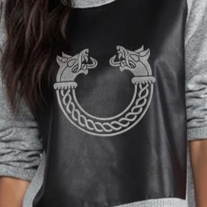 May include: A gray sweatshirt with a black panel featuring a silver embroidered design. The design depicts two stylized animal heads facing each other, connected by a braided, circular pattern. The sweatshirt has long sleeves.