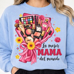 May include: Light blue sweatshirt featuring a bouquet of makeup products, including lipstick, eyeshadow, and perfume, tied with a pink ribbon. The text "La mejor MAMA del mundo" is displayed in red and white.
