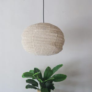 May include: A beige woven pendant light fixture hangs from a black cord against a white wall.