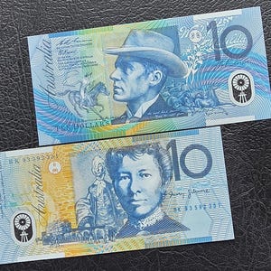 May include: Two Australian ten-dollar banknotes. The top note features a portrait of a man in a hat, with the text "TEN DOLLARS". The bottom note shows a woman's portrait. Both notes have the word "Australia" and the number "10".