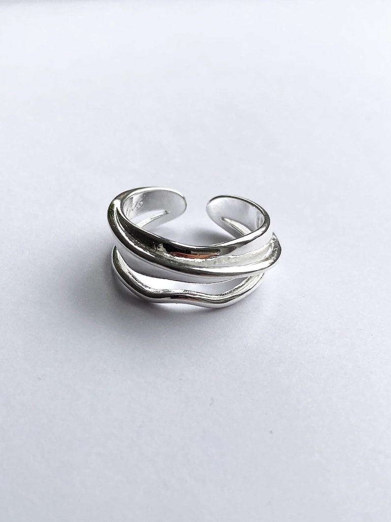 Pu&ograve; includere: Un anello color argento con un design a tre strati. L'anello ha una finitura liscia e lucida e un design aperto per la regolazione della taglia. Le fasce hanno una forma ondulata e organica, che aggiunge un tocco unico al gioiello. L'anello &egrave; d'argento.