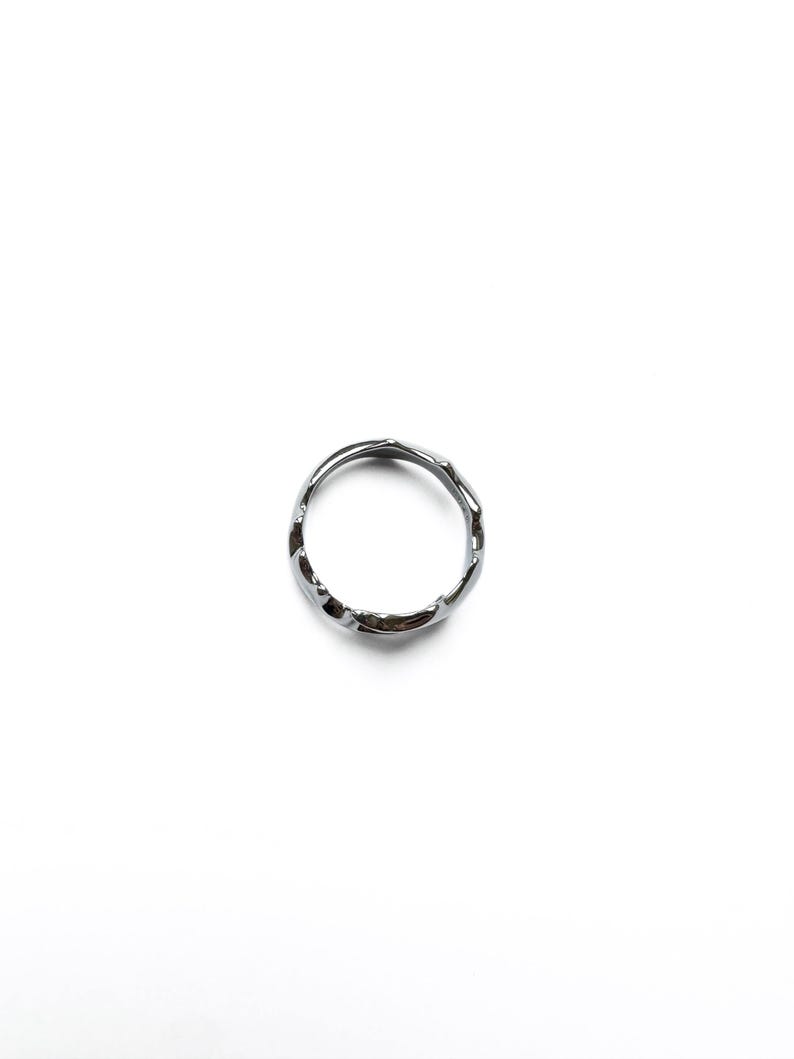 May include: A silver-colored ring with an irregular, textured surface. The ring is circular and appears to be made of metal. The design is minimalist and modern, suitable for everyday wear. The ring is shown against a white background.