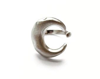 May include: A silver-colored crescent moon ear cuff. The ear cuff has a textured surface and a small ball at the end of the band. The design is minimalist and modern, suitable for everyday wear.
