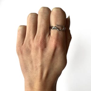 May include: A silver-colored ring with an organic, branch-like design. The ring is worn on a finger, showcasing its unique, nature-inspired aesthetic. The ring's open design adds to its modern appeal.