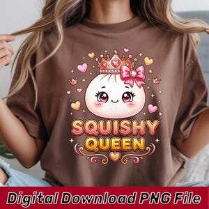 Może przedstawiać: Brązowy t-shirt z grafiką przedstawiającą białą, okrągłą postać pierożka w stylu kreskówkowym, noszącą złotą koronę i różową kokardę. Postać ma duże oczy i zaróżowione policzki. Poniżej znajduje się napis SQUISHY QUEEN pogrubioną czcionką.