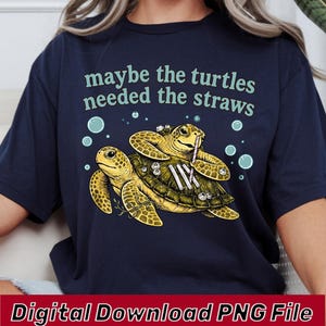 May include: A navy blue t-shirt featuring a graphic of two sea turtles with the text "maybe the turtles needed the straws" printed in light green above them. The turtles are depicted with small bubbles and striped straws on their shells.