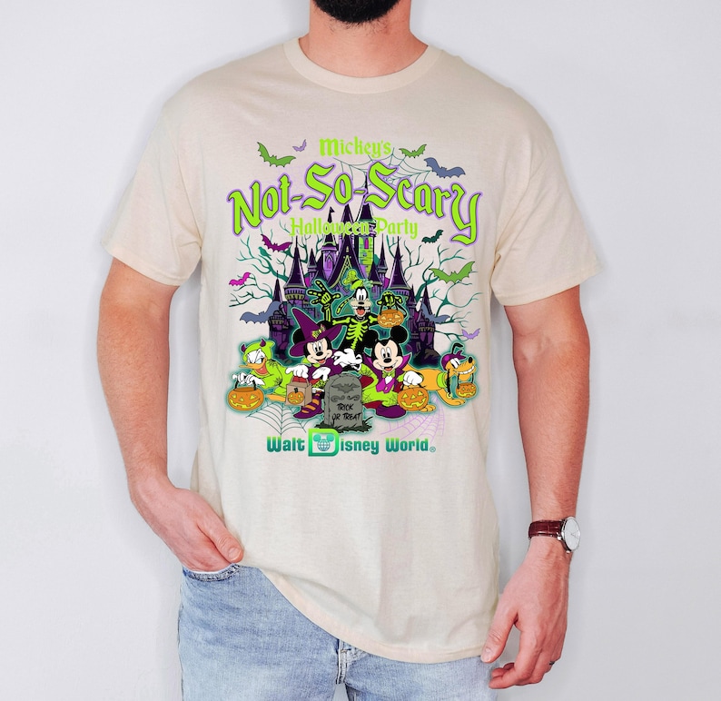 May include: Beige t-shirt featuring a colorful graphic for Mickey's Not-So-Scary Halloween Party at Walt Disney World. The design includes Mickey Mouse, Minnie Mouse, Donald Duck, and Goofy in Halloween costumes, with a spooky castle backdrop.