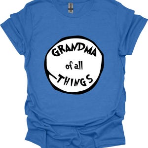 May include: A blue t-shirt with the text "GRANDMA of all THINGS" in a black and white circular design. The shirt is made of a soft material and has short sleeves. The text is in a playful, handwritten style.