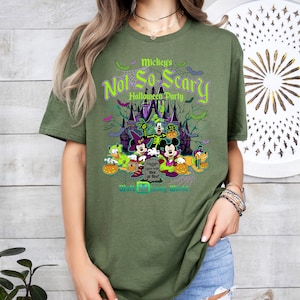 May include: Olive green t-shirt featuring a graphic for Mickey's Not-So-Scary Halloween Party at Walt Disney World. The design includes Mickey Mouse, Minnie Mouse, Donald Duck, and Goofy in Halloween costumes, with a spooky castle backdrop.