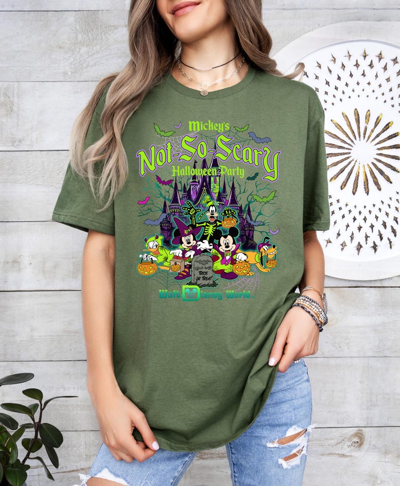 May include: Olive green t-shirt featuring a graphic for Mickey's Not-So-Scary Halloween Party at Walt Disney World. The design includes Mickey Mouse, Minnie Mouse, Donald Duck, and Goofy in Halloween costumes, with a spooky castle backdrop.