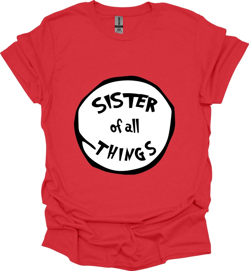 May include: A red t-shirt with the text "SISTER of all THINGS" in a black and white design. The text is inside a white circle with a black outline. The shirt is made of a soft material.
