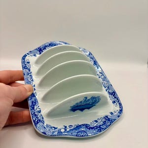 May include: A white ceramic toast rack with a blue floral pattern. It features five curved slots for toast. The blue and white design gives it a classic, vintage appearance. A decorative item for the breakfast table.
