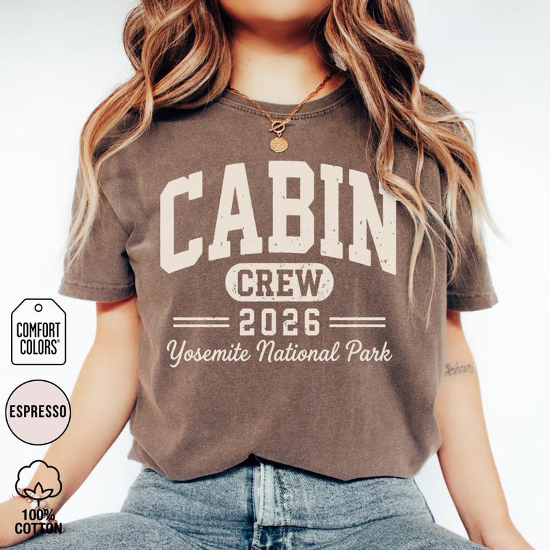 May include: An espresso-colored short-sleeve t-shirt featuring the cream-colored text CABIN CREW 2026 Yosemite National Park in a distressed collegiate font. The shirt includes a Comfort Colors brand tag and a 100% cotton label graphic.