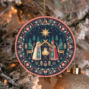 May include: Round Christmas ornament with a nativity scene design. The ornament features a dark blue background with a gold star, pine trees, deer, and floral patterns. The nativity scene includes Mary, Joseph, and baby Jesus. The ornament is trimmed with a red and white border.