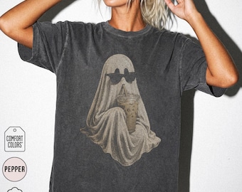 May include: A charcoal gray short-sleeve t-shirt featuring a graphic of a ghost wearing black sunglasses and holding an iced coffee drink. The shirt has a vintage-style washed finish and is labeled as 100% cotton by Comfort Colors in pepper.