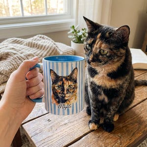 May include: A white ceramic mug with a black handle and the text "But First, Coffee" in a bold, black font. The mug is set against a blurred background, suggesting a cozy setting.