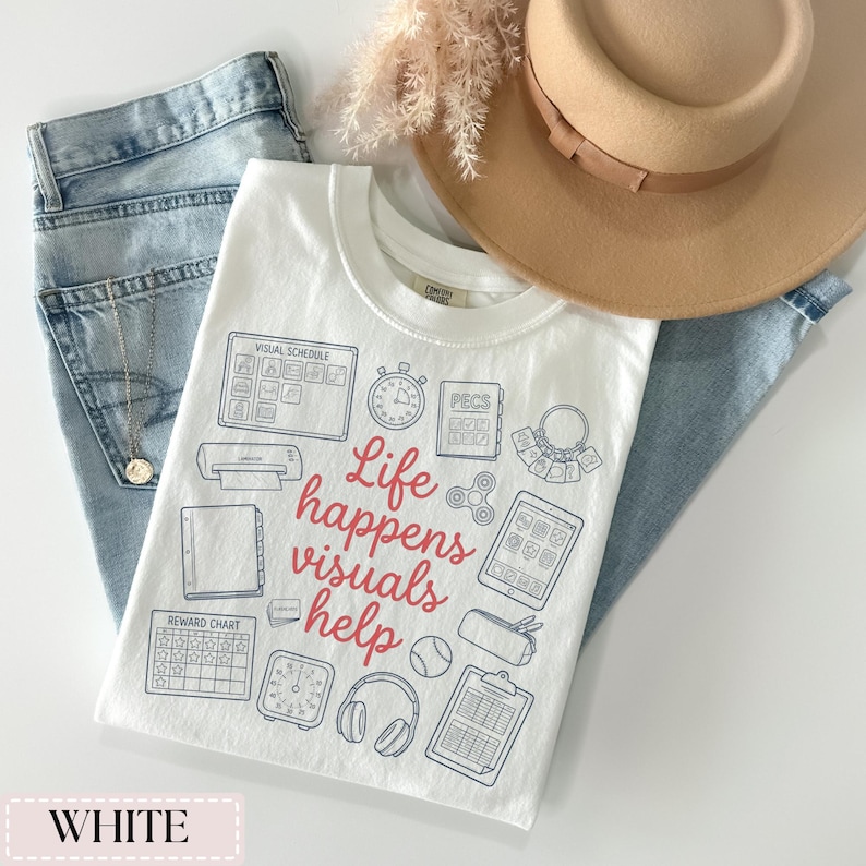 May include: White t-shirt with a crew neck featuring a graphic design with the text "Life happens visuals help" in red and blue. The shirt is paired with light blue jeans and a tan hat.