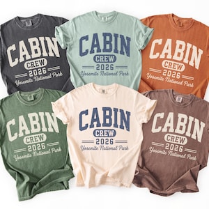 May include: Six short-sleeve crew neck t-shirts in charcoal, light green, orange, dark green, cream, and brown. Each shirt features the text CABIN CREW 2026 Yosemite National Park in a distressed navy blue and white collegiate-style font.