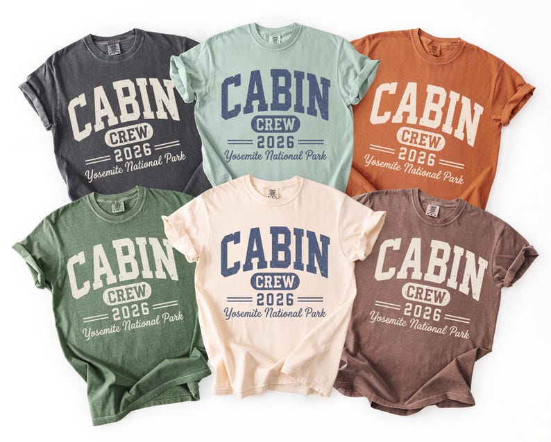 May include: Six short-sleeve crew neck t-shirts in charcoal, light green, orange, dark green, cream, and brown. Each shirt features the text CABIN CREW 2026 Yosemite National Park in a distressed navy blue and white collegiate-style font.