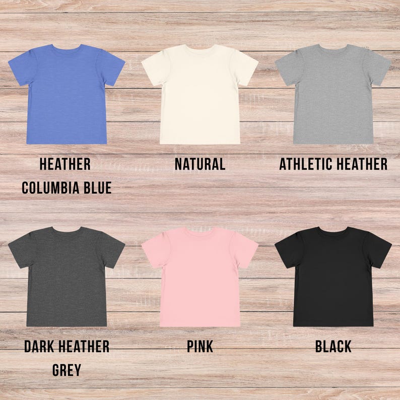 May include: Six short-sleeved t-shirts arranged in two rows. The top row features heather columbia blue, natural, and athletic heather colors. The bottom row displays dark heather grey, pink, and black colors. Each shirt has a crew neckline.