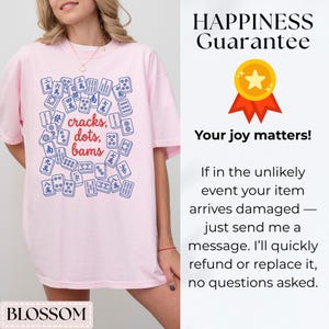 May include: A light pink t-shirt featuring a blue and white graphic of Mahjong tiles with the words "cracks, dots, bams." The shirt also has the word "BLOSSOM" at the bottom.