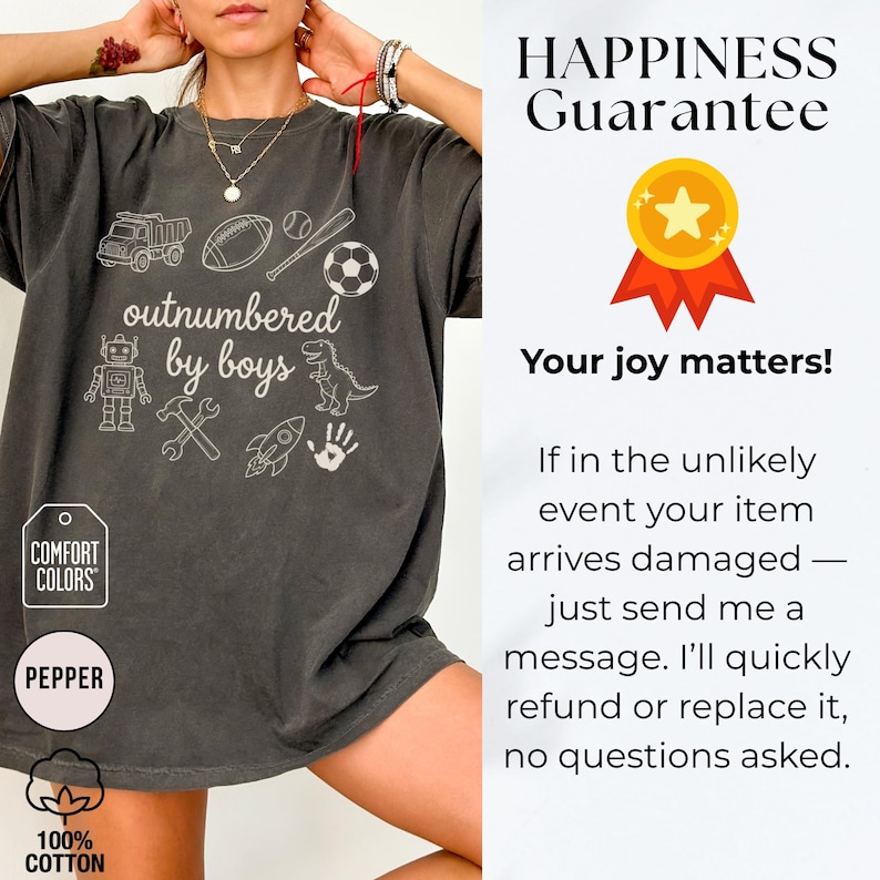 May include: Dark grey Comfort Colors t-shirt with the phrase "outnumbered by boys" and various white graphics including a truck, football, baseball, soccer ball, robot, dinosaur, and tools. The shirt is made of 100% cotton.