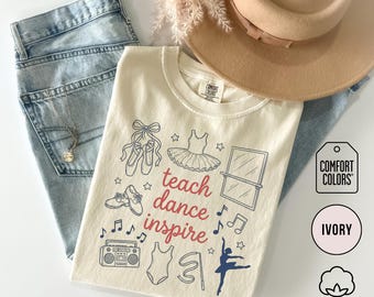 May include: Ivory-colored t-shirt with the words "teach dance inspire" and dance-themed illustrations. The shirt is paired with light-wash jeans, a necklace, and a tan hat. The shirt is made of 100% cotton.