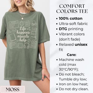 May include: A moss green t-shirt with the text "Life happens visuals help" and various white graphic icons. The shirt is made of 100% cotton and has a relaxed unisex fit.