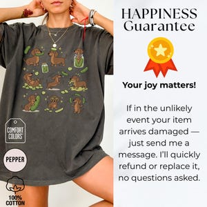 May include: Dark grey t-shirt featuring a playful design of dachshunds and pickles. The graphic includes various poses of the dogs with pickles. The shirt has the text "COMFORT COLORS" and "PEPPER" on it. Made of 100% cotton.