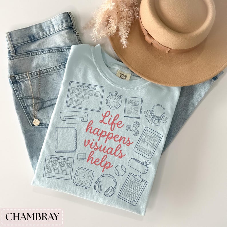 May include: A light blue t-shirt with the text "Life happens visuals help" and various graphic icons. The shirt is paired with light blue jeans, a tan hat, and a gold necklace. The word "CHAMBRAY" is at the bottom.