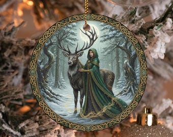 May include: Round Christmas ornament featuring a woman in a green hooded cloak and a stag in a snowy forest scene. The ornament has a gold-colored border with Celtic knot designs and a gold hanging chain. The background includes a full moon.