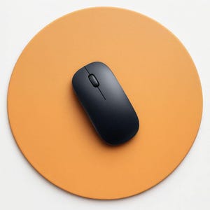 Könnte beinhalten: Eine schwarze, kabellose Computermaus liegt auf einem orangefarbenen, kreisförmigen Mauspads. Die Maus hat ein schlankes Design mit einem Scrollrad und zwei Tasten. Das Mauspad hat eine warme, orange Farbe.