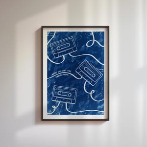 Può includere: Stampa artistica incorniciata con sfondo blu scuro, con tre illustrazioni di musicassette bianche e linee ondulate bianche. È incluso anche il testo "WHERE ONE STORY ENDS ANOTHER BEGINS". L'opera d'arte è in una cornice nera.