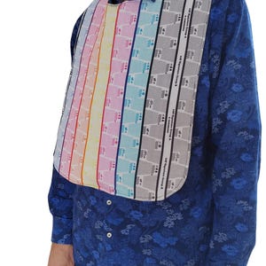 Peut inclure: Un bavoir coloré avec des rayures verticales aux couleurs de l'arc-en-ciel et grises. Le bavoir est porté sur une chemise bleue à motifs floraux. Le bavoir porte le texte "146 Signature Group B" et "146 Signature Group A".