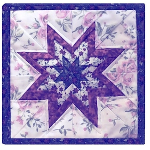 May include: A purple and white patchwork quilt with a star design. The quilt is made of different fabrics with floral patterns.