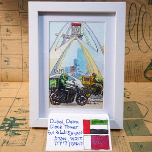 May include: A watercolor painting of the Deira Clock Tower in Dubai, United Arab Emirates. The painting shows the tower with a rainbow archway and two people riding motorcycles in the foreground. The painting is framed and has a small flag of the United Arab Emirates below it.