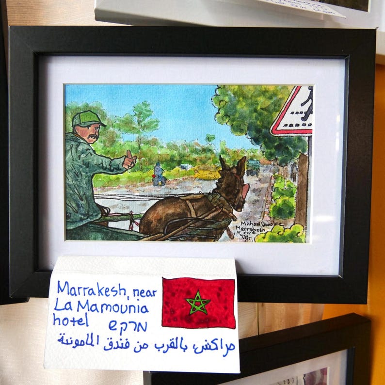 May include: A watercolor painting of a man in a green hat and brown jacket riding a donkey cart in Marrakesh, Morocco. The painting is framed and includes the text "Marrakesh, near La Mamounia hotel epan مراكش بالقرب من فندق المامونية".