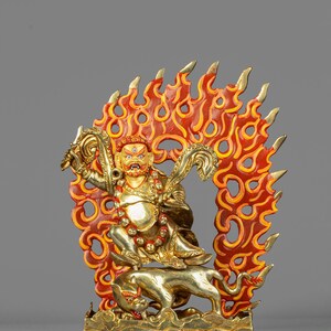 May include: A gold-colored statue of a deity with a fierce expression, adorned with jewelry, and seated atop a tiger. The deity is surrounded by a vibrant, red and yellow flame design. The statue is a representation of a religious figure.