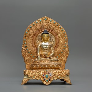 Peut inclure: Une statue dorée de Bouddha en position méditative. La statue est ornée de turquoise et d'autres pierres précieuses colorées. Les détails complexes du trône et du halo dorés sont visibles, créant un sentiment de sérénité et de signification spirituelle.
