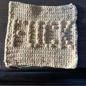 May include: A white crocheted dishcloth with a textured design. The dishcloth has the word "PUD" written in raised letters.