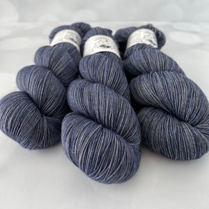 May include: Six skeins of yarn in a deep blue color with subtle gray highlights. Each skein is neatly wound and labeled, suggesting a high-quality crafting material. The yarn appears soft and suitable for knitting or crochet projects.